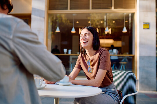 Two young people enjoying a coffee break at an outdoor cafe, a radiant woman smiling during social interaction