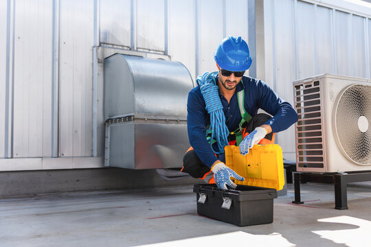 Maintenance engineer man in safety harness preparing tools for industrial rooftop service, Professional HVAC technician opening toolbox to repair air conditioning units on rooftop