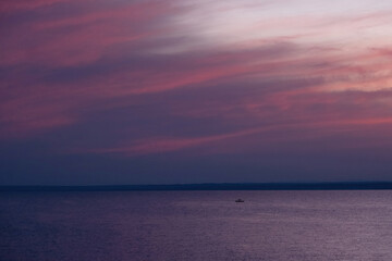 Obraz premium A minimalist seascape at twilight featuring a vast purple and pink sunset sky over calm water with a tiny boat on the horizon. 