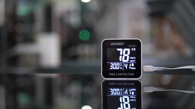 Close-up of modern digital PM 2.5 detector showing unhealthy air quality levels on reflective black surface