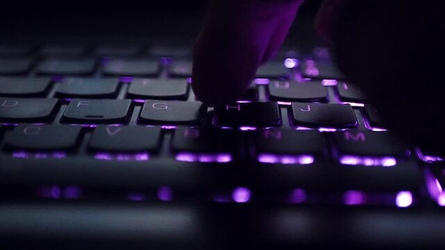 Close-up of a persons hands typing on a colorful backlit keyboard in the dark.