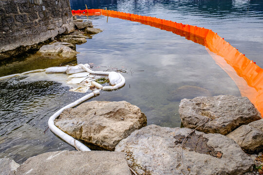 Oil containment booms are used to manage water pollution in a lake during winter near a small town in the background with mountains visible
