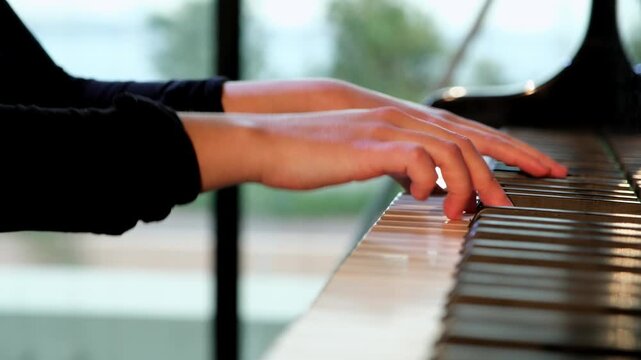 Pianist hands playing a classical grand piano melody with skilled fingers on the keyboard, professional musician practicing a concert performance with natural light