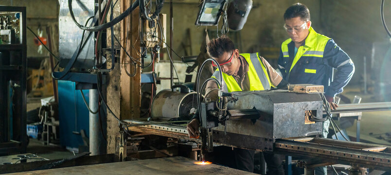 Two Male Engineers Operating CNC Machine with Sparks Flying Engineers Teamwork in Controlling Automated Cutting Machine Mentor and Technician Learning CNC Operation in a Dusty Environment.