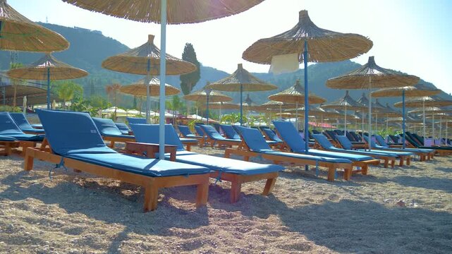 Seaside view with rows of lounge chairs and thatched umbrellas. Peaceful coastal atmosphere with no people. Ideal destination for summer holiday and relaxation. Perfect setting for leisure. Empty sun