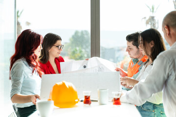 A team of architects, engineers, and project managers review building plans and blueprints, with a focus on occupational health and safety, in a modern office setting. © bulentbaris