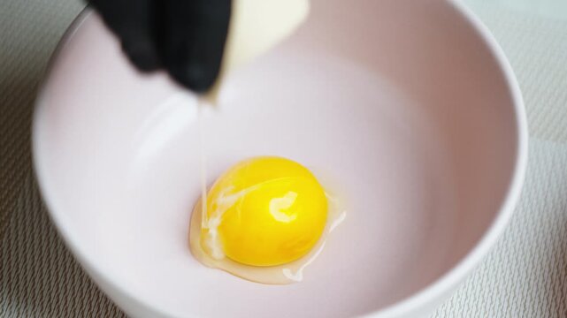 Cracking egg shell carefully. Detailed view of hand cracking egg into ceramic bowl in clean kitchen setting