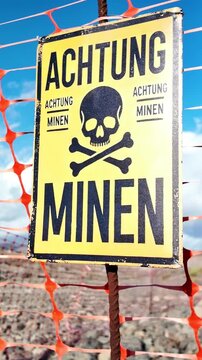 Old yellow german sign warning of the presence of mines with a skull and crossbones symbol, marking a restricted area with an orange plastic fence and indicating extreme danger from explosives