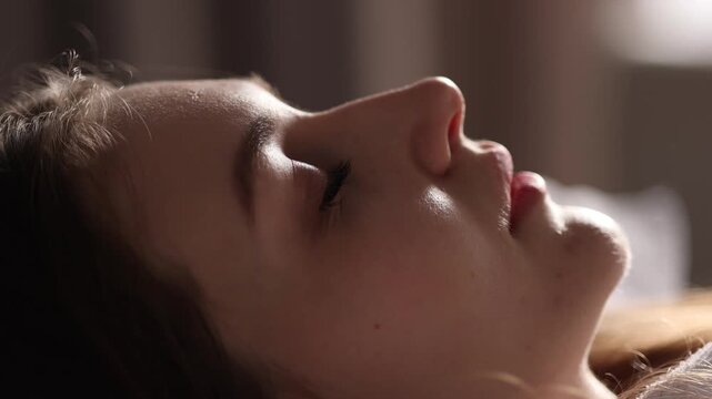 Close up of young woman lying in bed suddenly waking up and opening eyes. Morning awakening, emotional reaction, lifestyle and sleep concept in soft light.