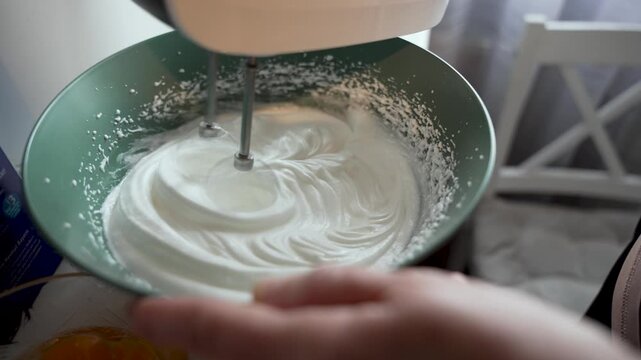 A thick glossy meringue rises under electric beaters in a bowl during cake or dessert preparation.
