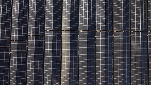 Rows of solar panels arranged in a grid pattern, showcasing the gradual transition of light across the surface, highlighting their sleek design and structure in a solar farm setting