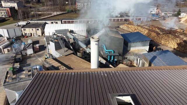 Industrial facility with smoke rising from chimney, showcasing machinery and wood piles in a manufacturing setting