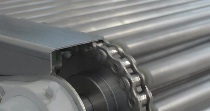A stainless steel conveyor belt moves, driven by a chain transmission. Close-up handheld indoors shot, real time speed.