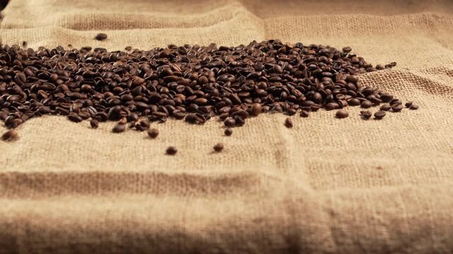 Slow motion. fresh roasted coffee beans falling onto textured burlap sack