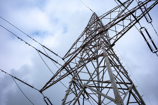 High-voltage power pylons against a cloudy sky. Distribution of electrical power via an overhead wire line.