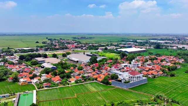 High angle aerial view of a rural village with red tile roofs and lush green rice fields in Indonesia during a sunny day