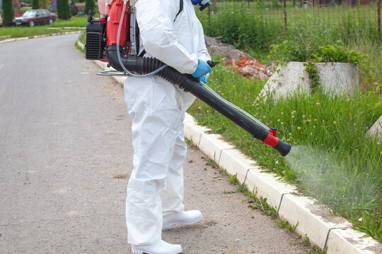 Pest control worker spraying herbicide on overgrown roadside grass in protective suit