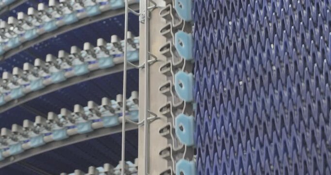 A multi-tiered spiral conveyor in operation, plastic mesh belts moving in different directions. A working transport system with an axisless spiral. Close-up handheld indoors shot, real time speed.
