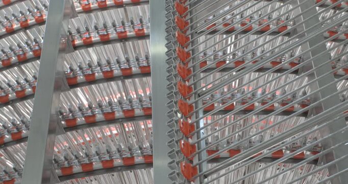 A multi-tiered spiral conveyor in operation, stainless steel mesh belts moving in different directions. A working transport system with an axisless spiral. Close-up handheld indoors shot, real time sp