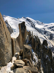 Rugged arête des cosmiques and rock formations in the high alps, with impressive snow-capped peaks of the Mont Blanc massif stretching into a clear blue sky - stock photo