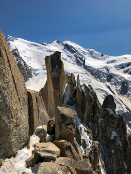 Rugged ar&ecirc;te des cosmiques and rock formations in the high alps, with impressive snow-capped peaks of the Mont Blanc massif stretching into a clear blue sky - stock photo