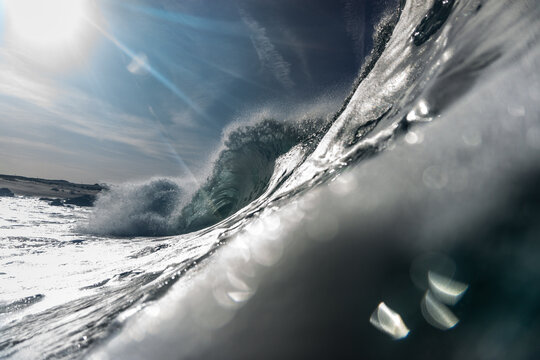 Dynamic closeup of a breaking wave under a dramatic sky, capturing swirling water, bright reflections, and coastal energy in a moody, immersive seascape scene.