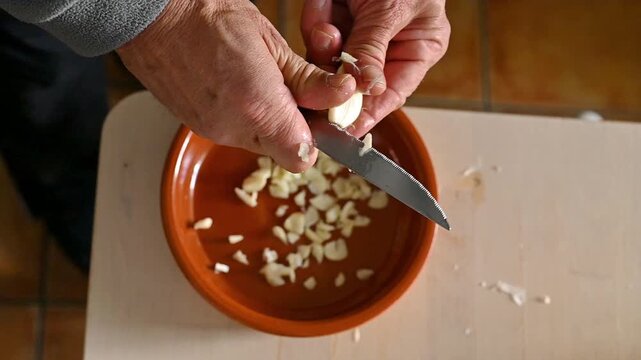Overhead view adding sliced garlic into clay dish for Spanish tapas cooking traditional small plates food concept