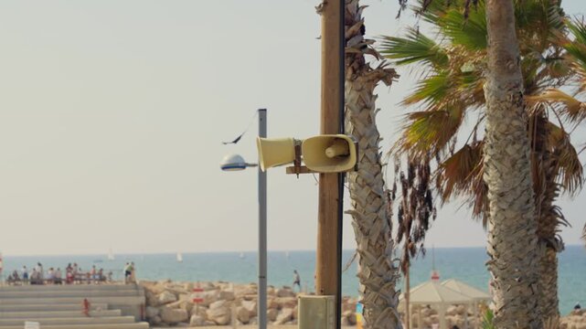 Megaphone loudspeaker for public announcements siren or alarm in Tel Aviv Israel. Situated on wooden pole stand is PSA loudspeaker. In background is sea or beach with swimmers and bathers in water