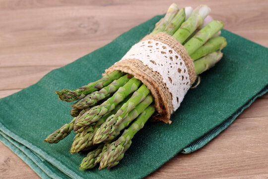 Frischer gr&uuml;ner Spargel im Jutebund mit Spitzenborte auf einem gr&uuml;nen K&uuml;chentuch.