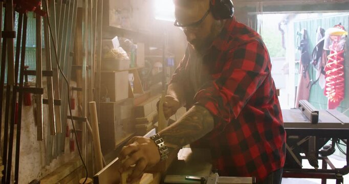 Woodworking process. Jointer machine. Carpenter man with ear protectors pushing long plank with hand pad on professional power equipment.