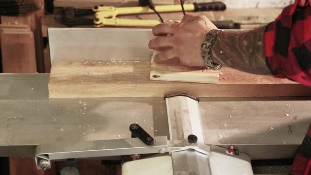 Woodworking process. Jointer machine. Carpenter hand guiding long plank with push pad block on professional power electric equipment.