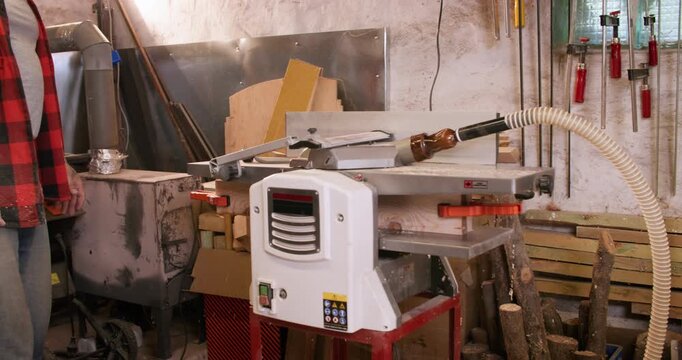 Lumber plank making. Joinery technology. Carpenter putting pair of wooden block in thickness planer preparing material for furniture.
