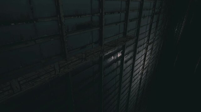 Narrow grated pathway with faint glow, ventilation ladder and access hatch leading into crawlspace, drone maintenance signs and condensation on steelwork,