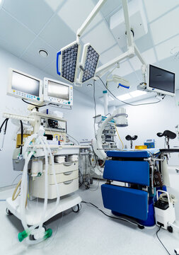 Empty modern operating room with surgical lights and equipment. Interior of sterile surgical theater featuring anesthesia workstation, blue table and overhead lamps.