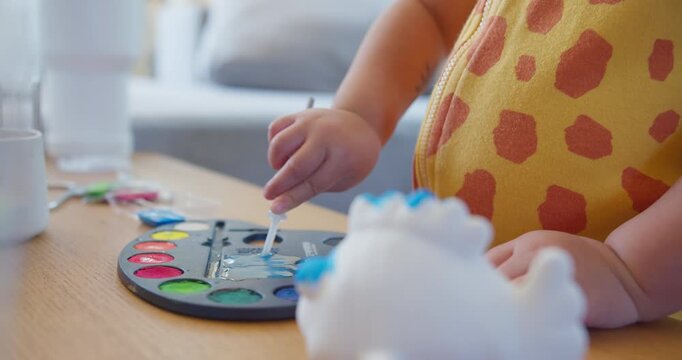 Young toddler uses a water dropper on a colorful paint palette at a home table, focusing on early childhood education, fine motor skill development, and creative indoor playtime.