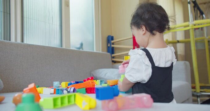 Toddler builds with colorful plastic blocks on a gray sofa in a brightly lit home environment, focusing on early childhood development, creative learning, and safe domestic play.