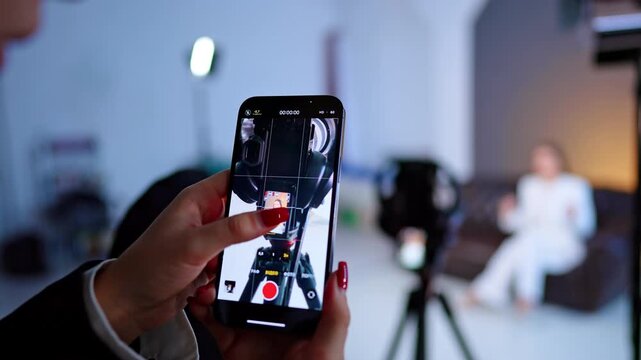 Female hands hold the phone taking video. Display of camera on tripod in focus.