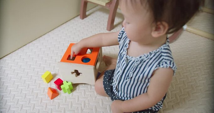 Curious toddler places colorful blocks into a wooden shape sorter on a textured playroom mat, focusing on early childhood development, cognitive learning, and fine motor skills.