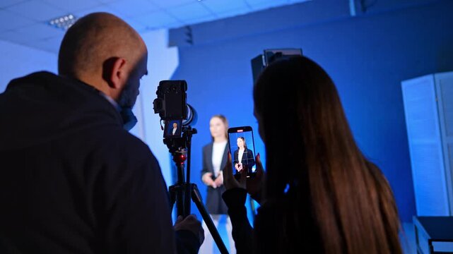 Rear view of a man and woman taking video in photo studio. People work backstage at blog footage.