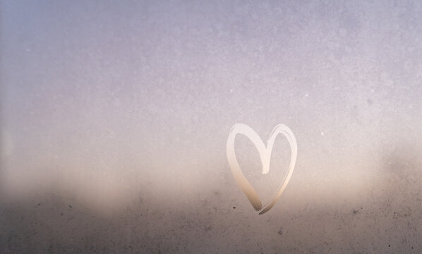 Romantic blurred texture of a misty window with a hand-drawn heart at sunset