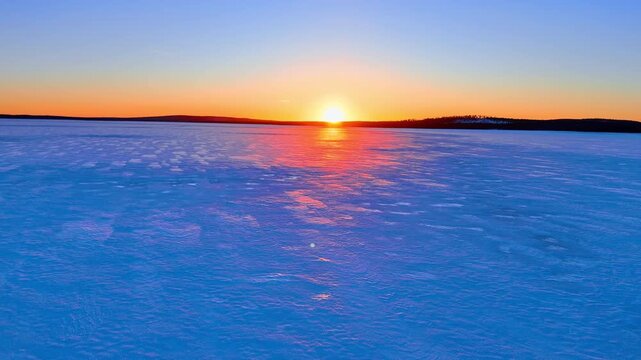 Bright sun setting over flat frozen horizon of arctic lake. Symmetrical aerial shot of the sun over a vast snow covered ice field at sunset.