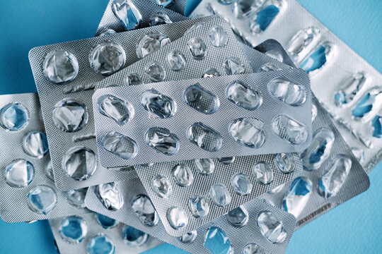 Collection of used medication blister packs lies scattered on blue surface. Non-recyclable medical waste, plastic pollution in healthcare, eco-friendly pharmacy trends.