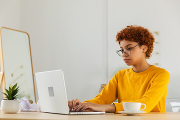 Fototapeta premium African american girl using laptop at home office looking at screen typing chatting reading writing email. Young woman having virtual meeting online chat video call conference. Work learning from home