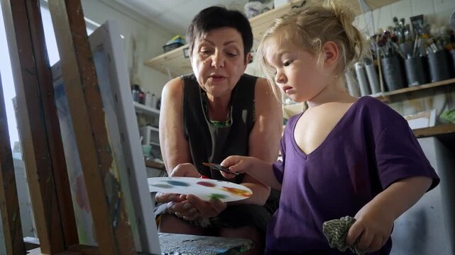 Child painting with an grandmother in a cozy art studio. Candid indoor moment of creativity and learning. Artistic lifestyle scene with real people and natural light.
