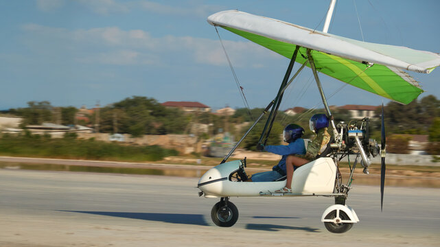 An ultralight aircraft (motorized hang glider) on a runway with a resort village in the distance. Aerial tour with a passenger.