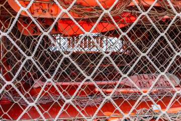 Close-up shot block island life raft with white rope net draped over orange survival equipment, including oars and floatation devices, on a boat.