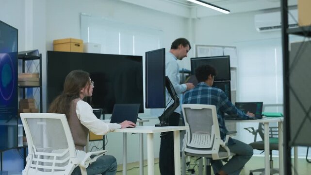 professional woman with glasses in modern AI development office focuses intently on coding at laptop while viewing large blue AI Assistant screen with glowing neural brain graphic, symbolizing machine