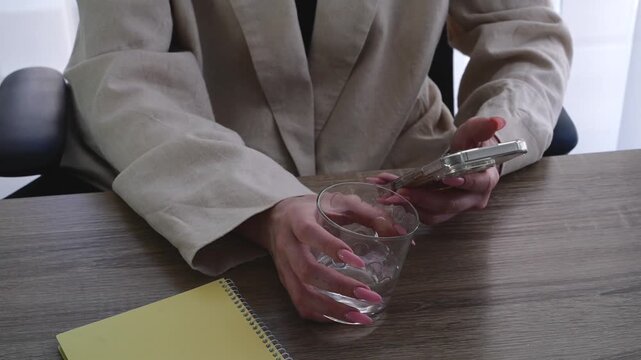 A woman holding a glass of water while sitting in an office.
Relaxing at work.
A tired woman drinks water and texts on her phone.
Working space and a woman in a light-colored jacket using a mobile pho