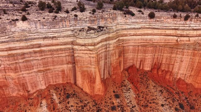 High cliff wall with distinct horizontal sedimentary layers. Detailed view of a massive geological wall showing color transitions from white to red rock.