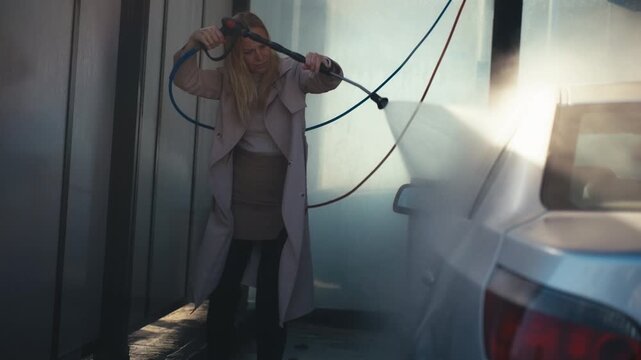 Young business woman cleaning her car with pressure washer at self service station. Urban lifestyle and daily routine. Concept of independence and self care.